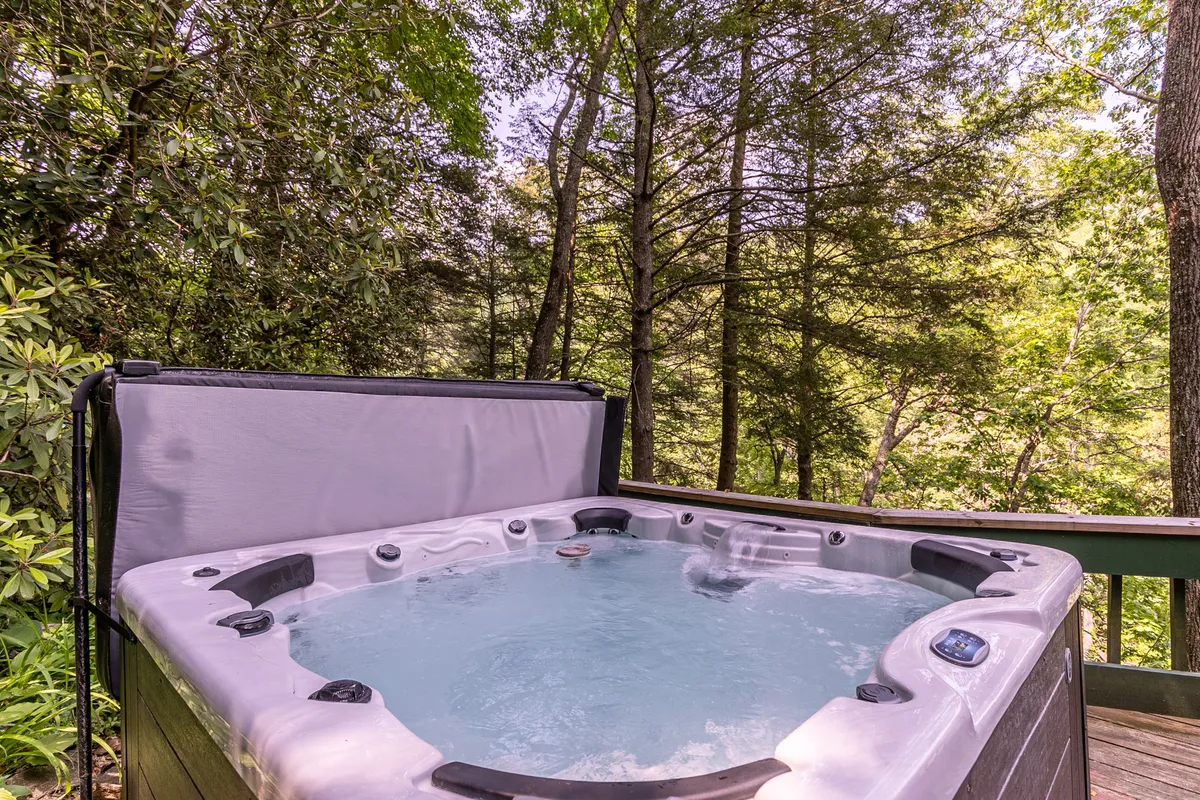 This image features a hot tub on a deck surrounded by trees, with relaxing seating and a view of nature. The scene is inviting, suggesting opportunities for group relaxation and enjoyment in a beautiful mountain setting.