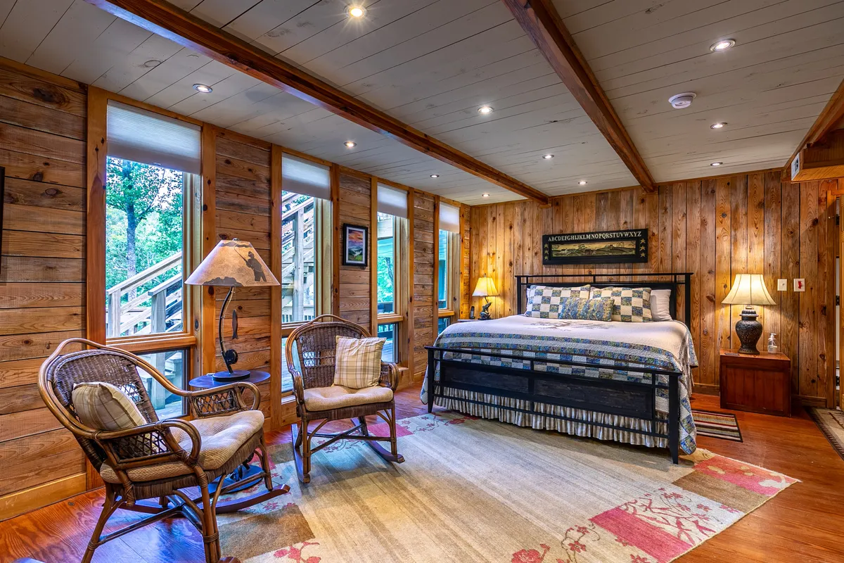 A serene bedroom featuring a generously sized bed, cozy armchairs, soft lighting from bedside lamps, and a plush area rug. The windows allow soft natural light to filter in, creating a calming atmosphere perfect for relaxation or enjoying a quiet morning coffee.